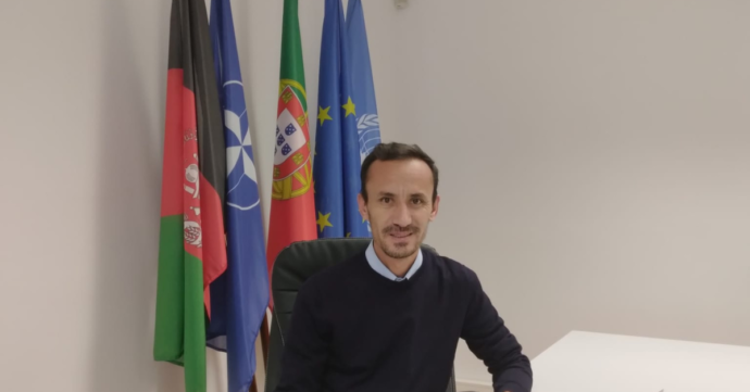 Ziau, advocate for refugees' integration and active point of contact for Afghan refugees in Portugal, sitting and smiling at the camera. On this back, there are the Portuguese, Afghan, European flags.